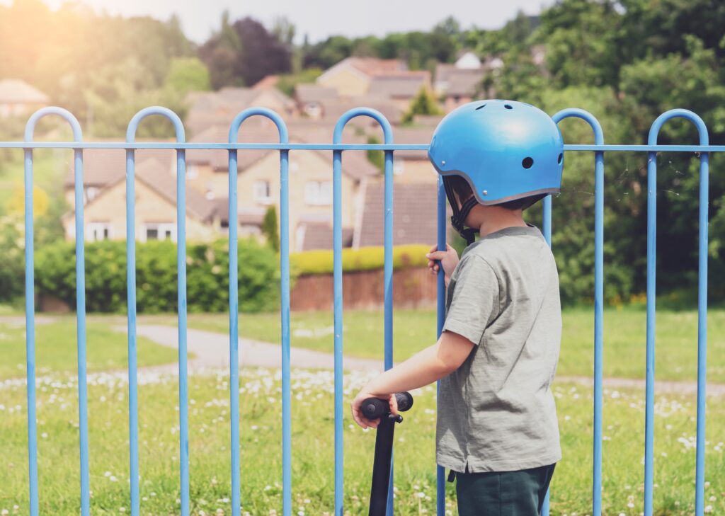 rear view portrait ofsad little boy looking through metal fence